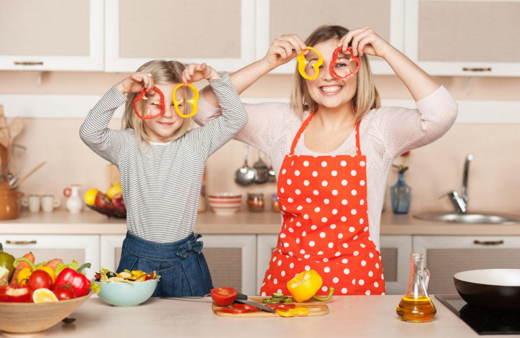 Mother and daughter holding red and yellow cut up peppers in front of their eyes
