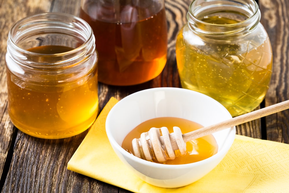 Different varieties of honey in three glass jars on a wooden background.