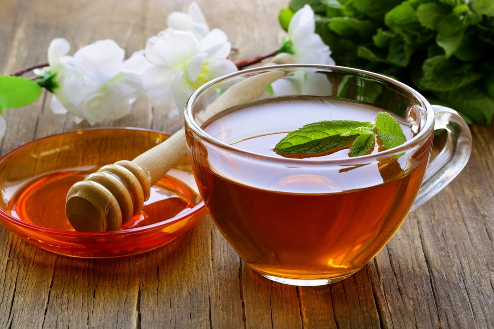 A cup of tea with mint and honey on a wooden table.