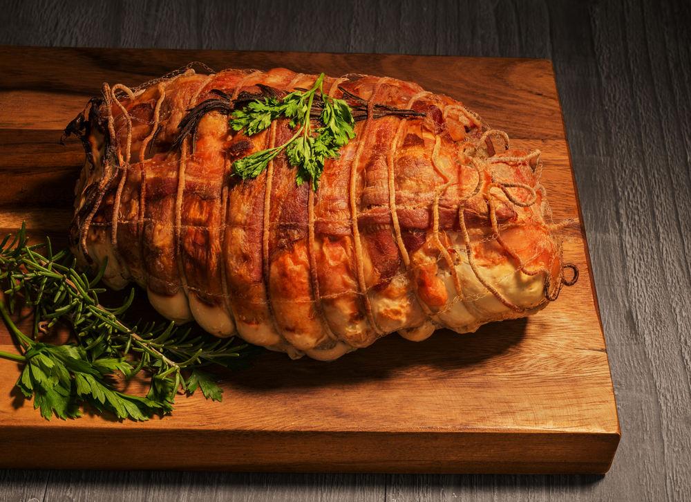 Stuffed turkey wrapped in bacon and garnished with herbs on a wooden board.