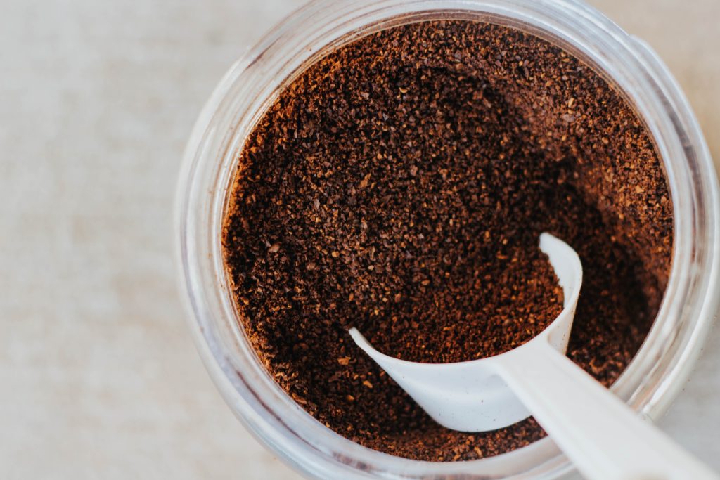 overhead shot of glass container filled with coffee grounds and white scoop
