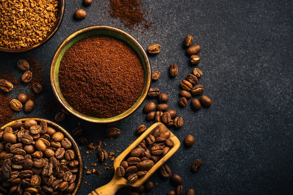Coffee beans, ground coffee, and instant coffee in bowls on a dark table