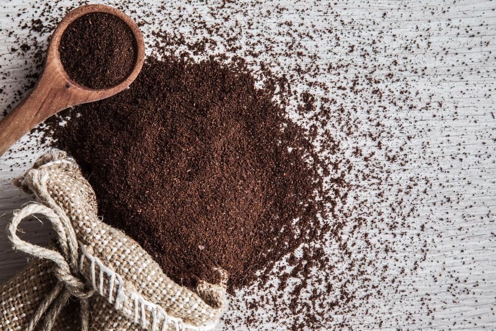 Coffee grounds spilling from a burlap sack and wooden spoon onto a table