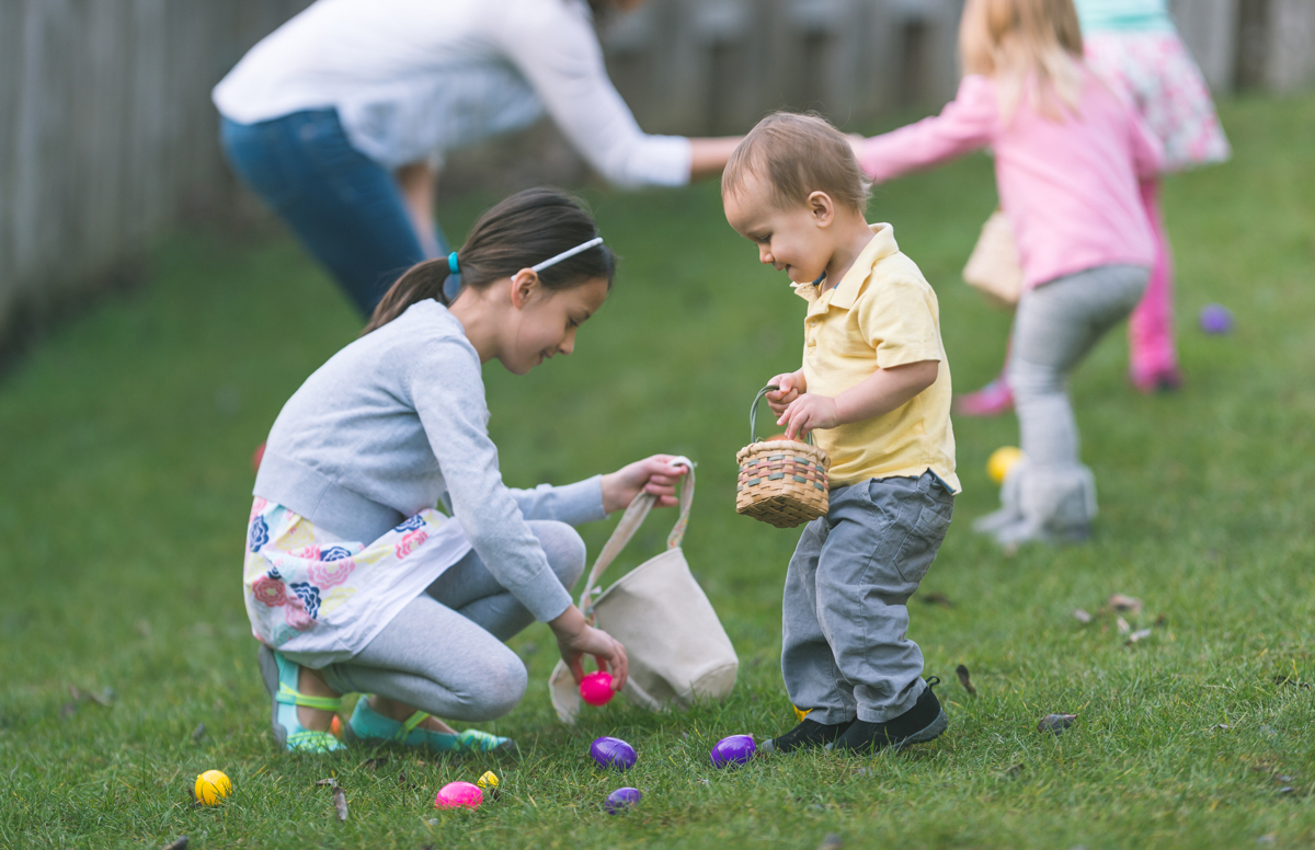 young girl and toddler boy picking up Easter eggs in baskets