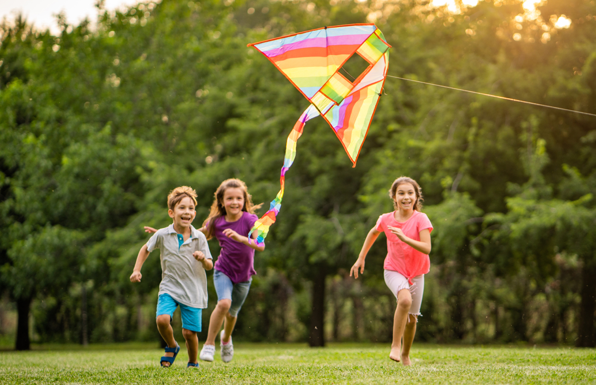 two young girls and a young boy flying a colorful kite in a park