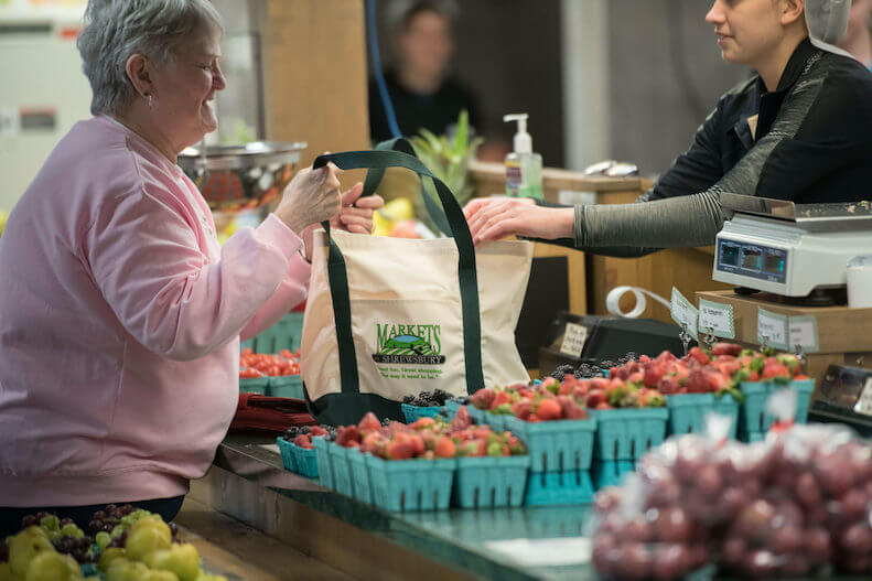 An older woman buys fresh strawberries at market
