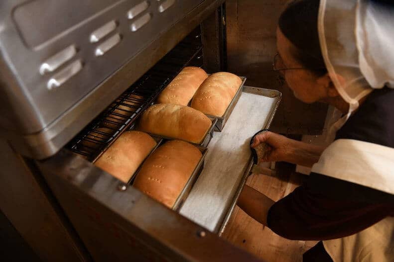 Amish woman removing homemade bread from oven at the Markets at Shrewsbury in Glen Rock, York County, Pennsylvania