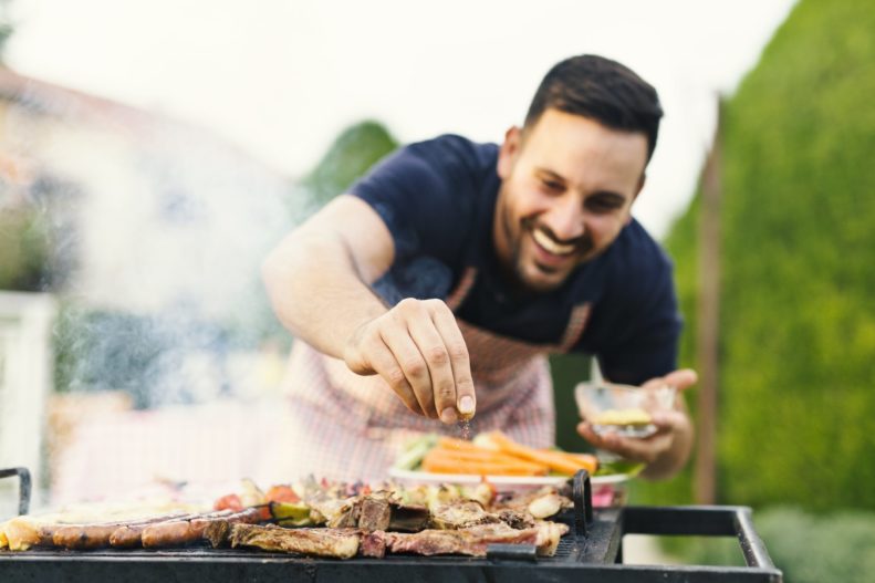 Man grills pieces of steak and seasons them.