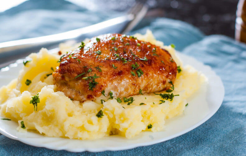 A piece of cooked chicken on top of mashed potatoes.