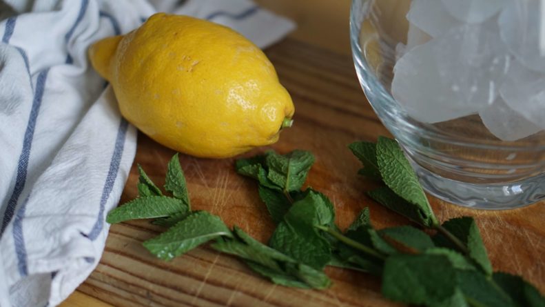 A lemon and fresh mint sit on a wooden cutting board, waiting to be made into tea.