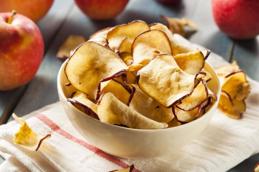 Fresh apple chips sit in a white bowl on the counter.