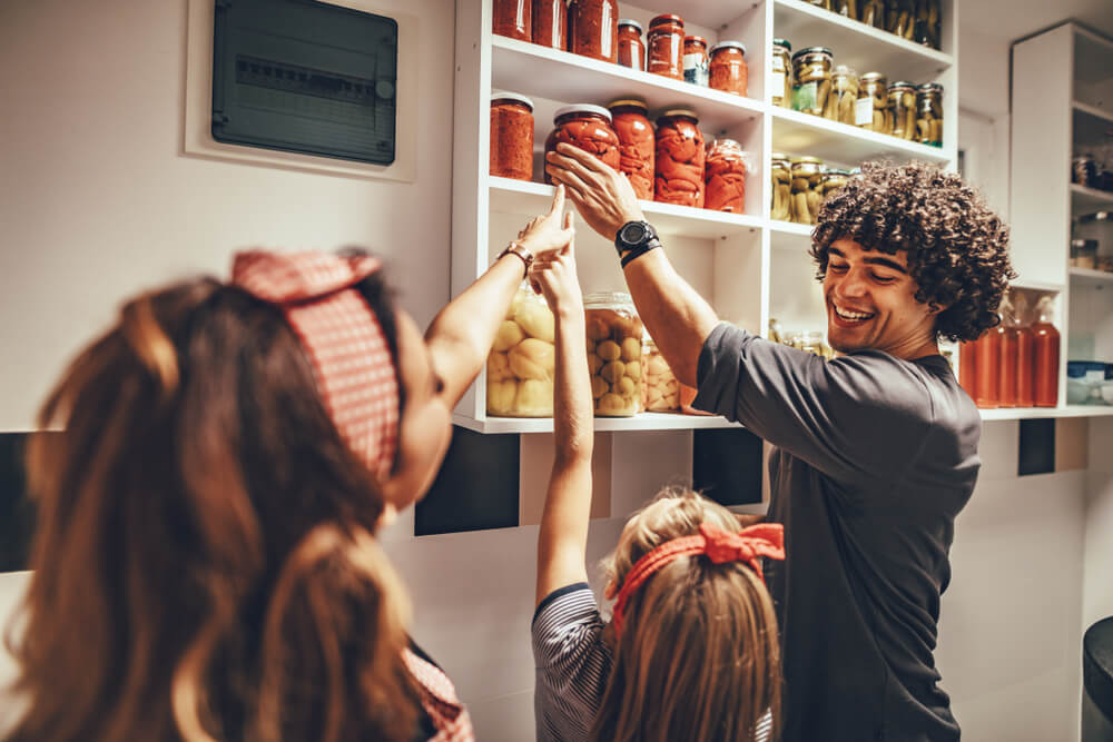 A dad reaches up to grab a jar of preserved red tomatoes for his daughter and wife.