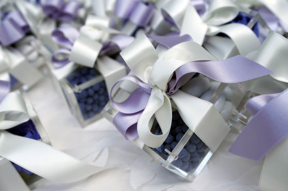 Clear boxes filled with purple candy sit on a wedding candy table.