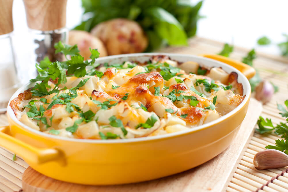 Fresh gratin potatoes are served inside a bright yellow stoneware casserole dish.