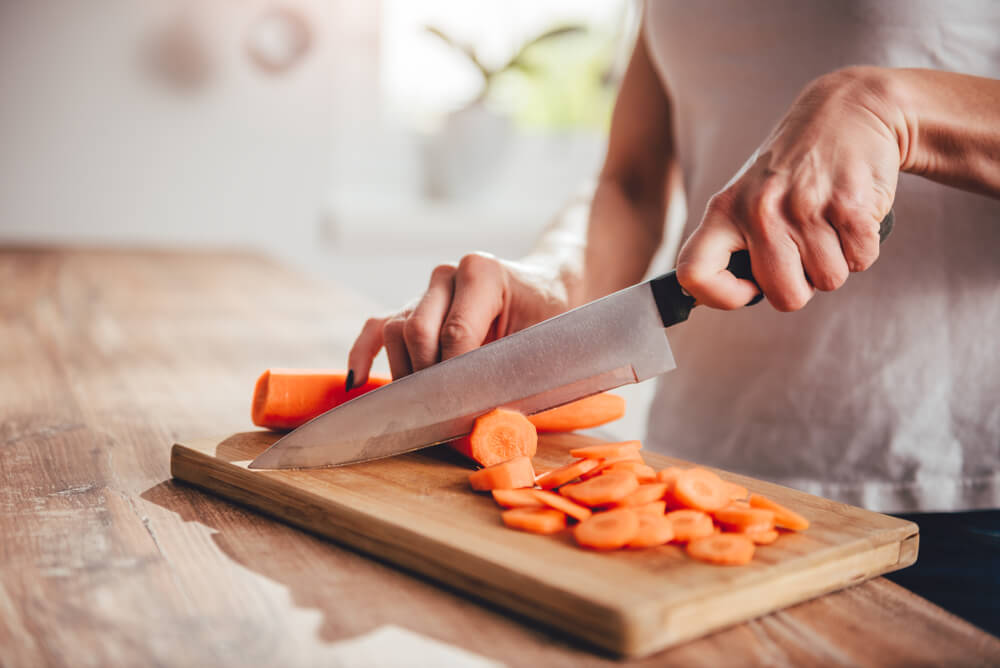 A woman slices large carrots on a cutting board.