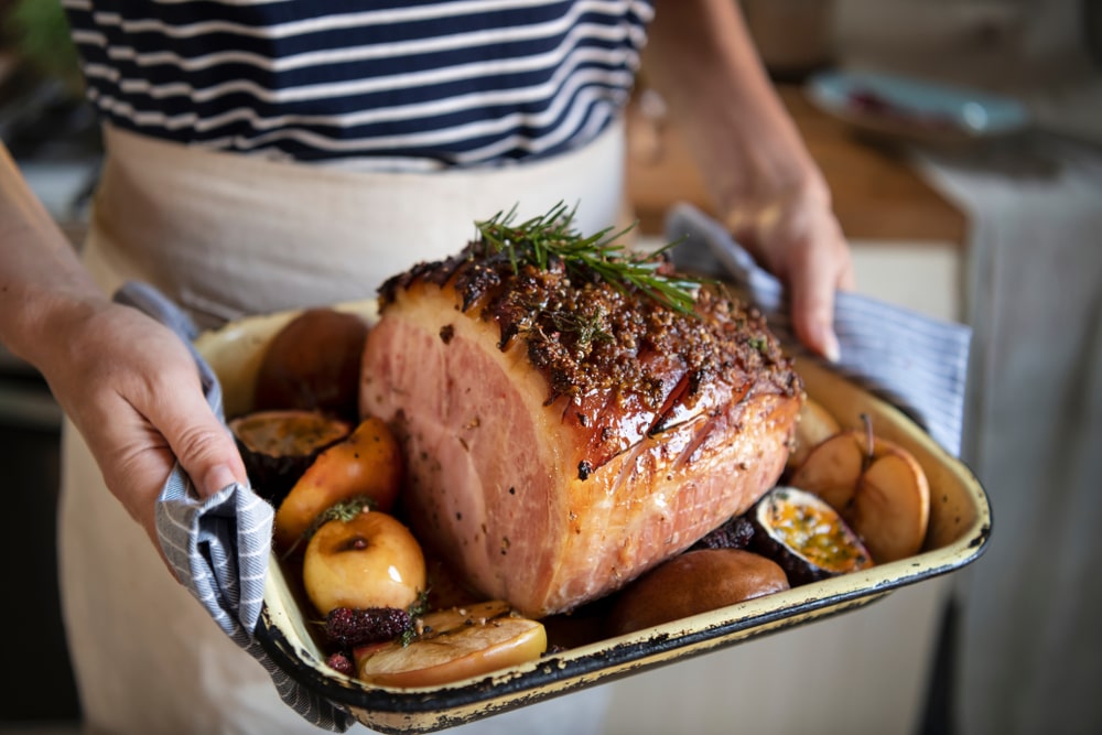 A woman holds a fresh baked ham.