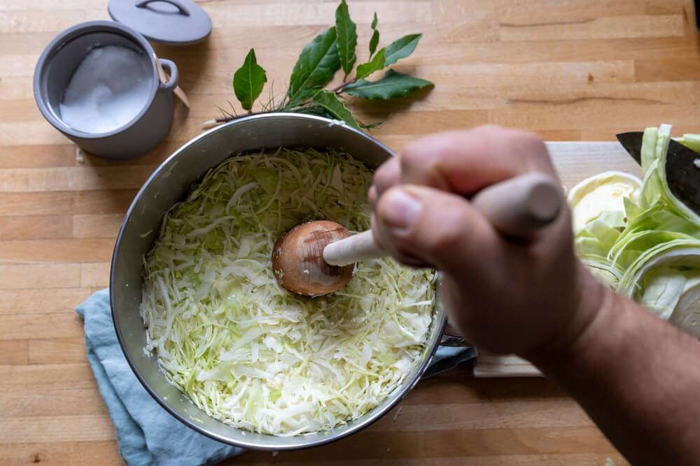 Person using a mortal and pestle to grind cabbage for Pennsylvania Dutch Sauerkraut 