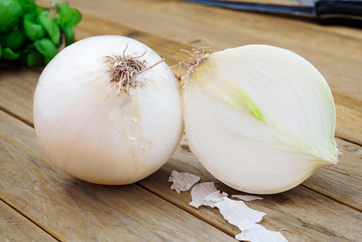 a full white onion next to a halved white onion
