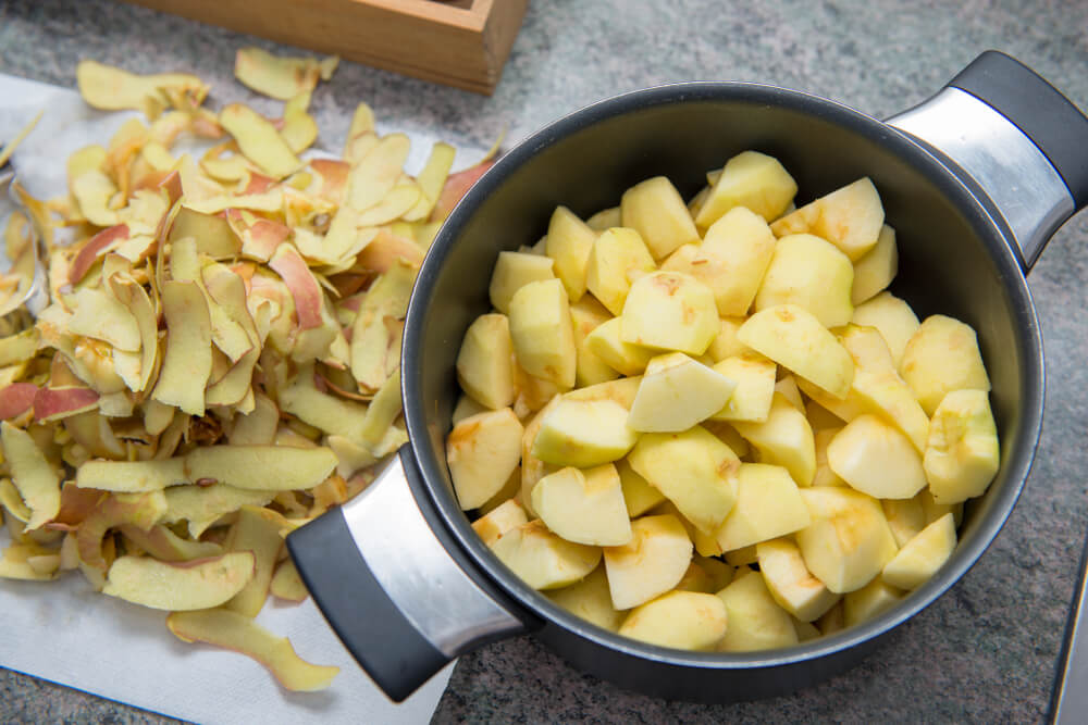 a pot of apples that are peeled and sliced next to a pile of the scraps from the apple skin