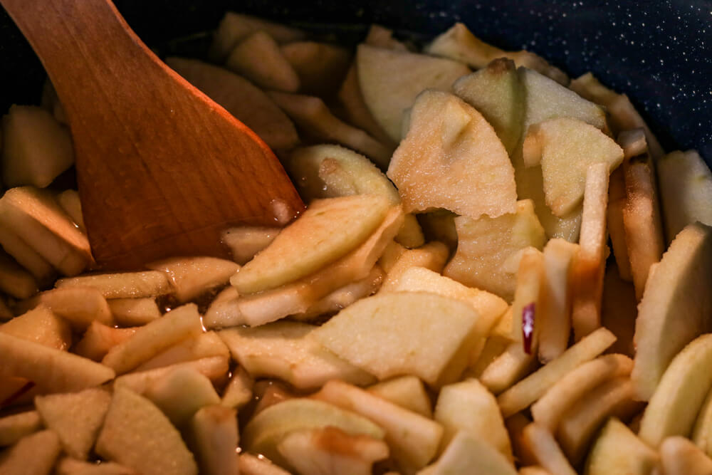 a close up of peeled and sliced apples being tossed in a pan with cinnamon and brown sugar