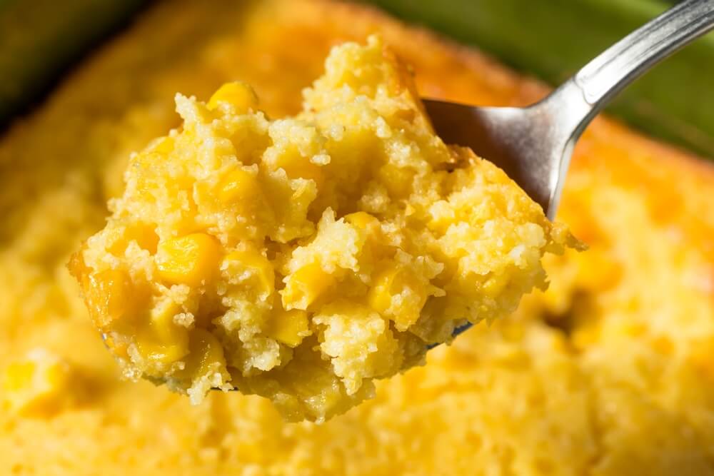 a close up of sweet corn pudding on a spoon with the rest of the casserole blurred in the background