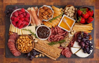 a charcuterie board with meats, cheeses, crackers, almonds, fruit, honey, and other snacks