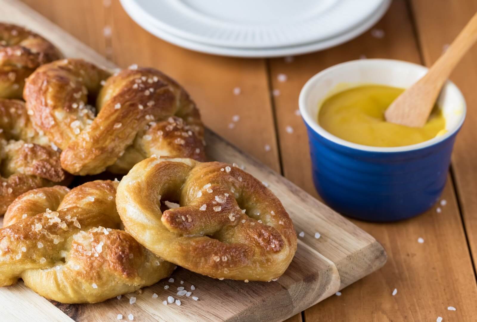 some freshly baked soft pretzels sitting on a wooden platter next to a small dish of mustard