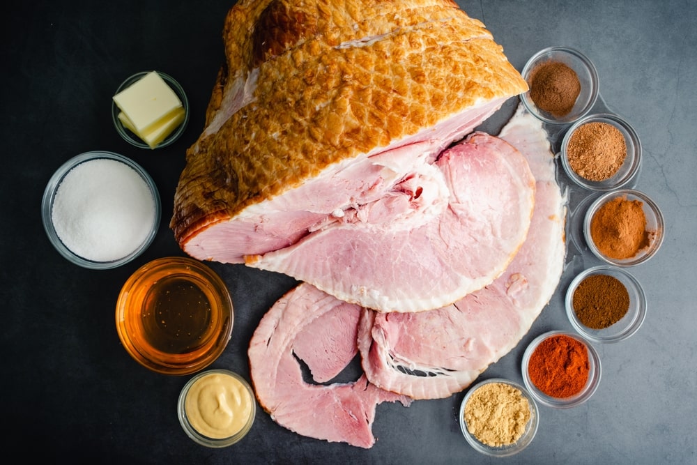 An entire ham surrounded by a variety of small ingredient bowls used to make a glaze.
