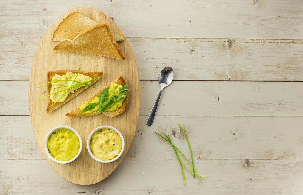 Toast with Dutch curried chicken egg salad on an wooden oval plate.